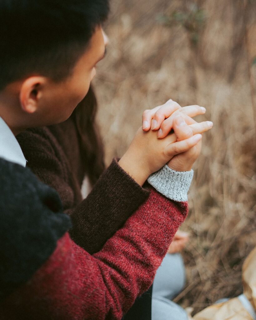 Como a humildade transforma conflitos conjugais: a man sitting in a field holding his hands together